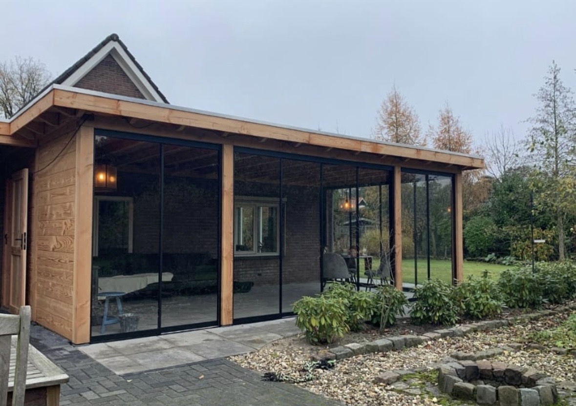 Houten overkapping met glazen schuifwanden, terras en groene beplanting