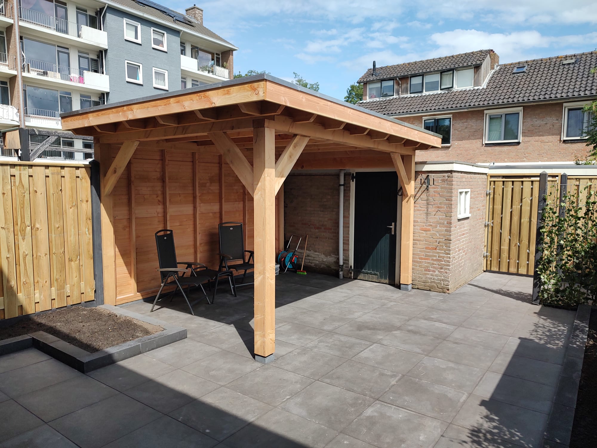 Houten overkapping met groot terras, schutting en nette bestrating